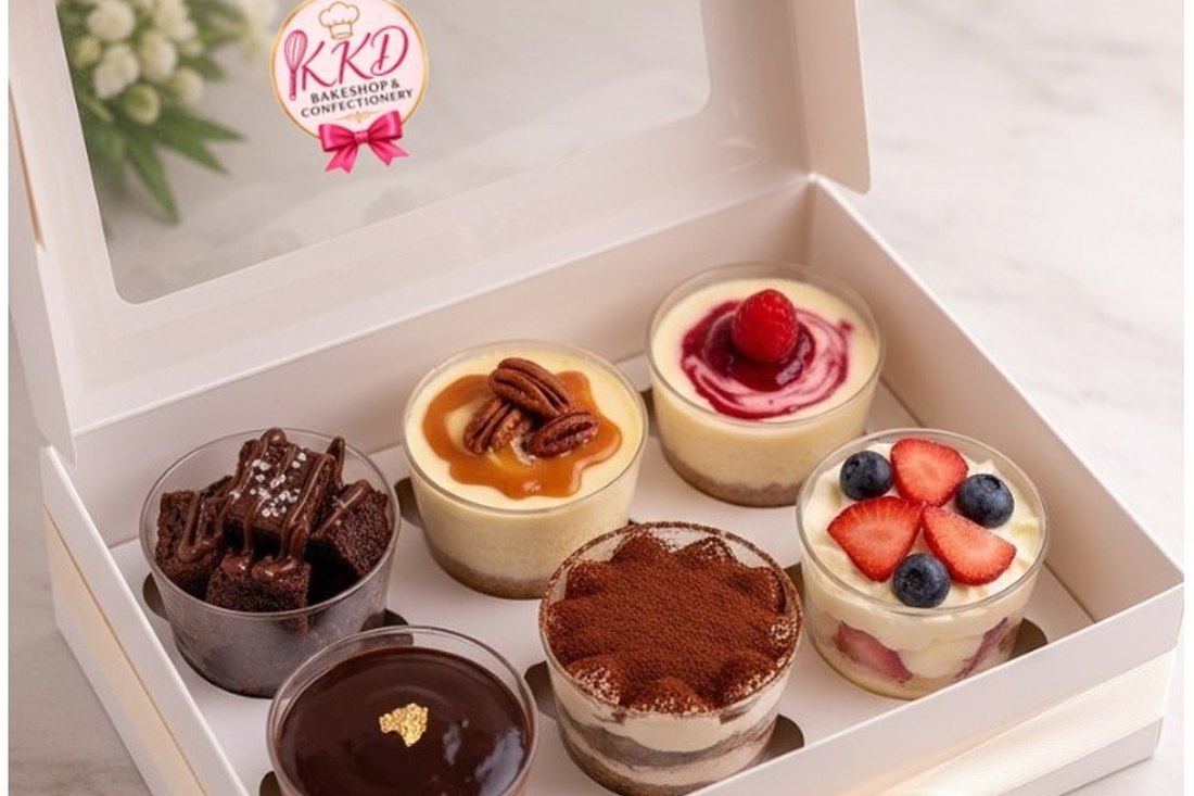 The KKD Dessert Tasting Box: six tasting portions in clear cups, brownie, two cheesecakes, chocolate mousse, tiramisu and a berry parfait, in a white KKD box tied with a ribbon