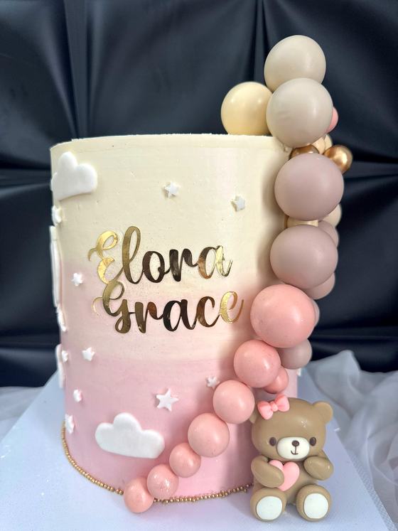 Pink ombre celebration cake with a balloon garland and teddy topper