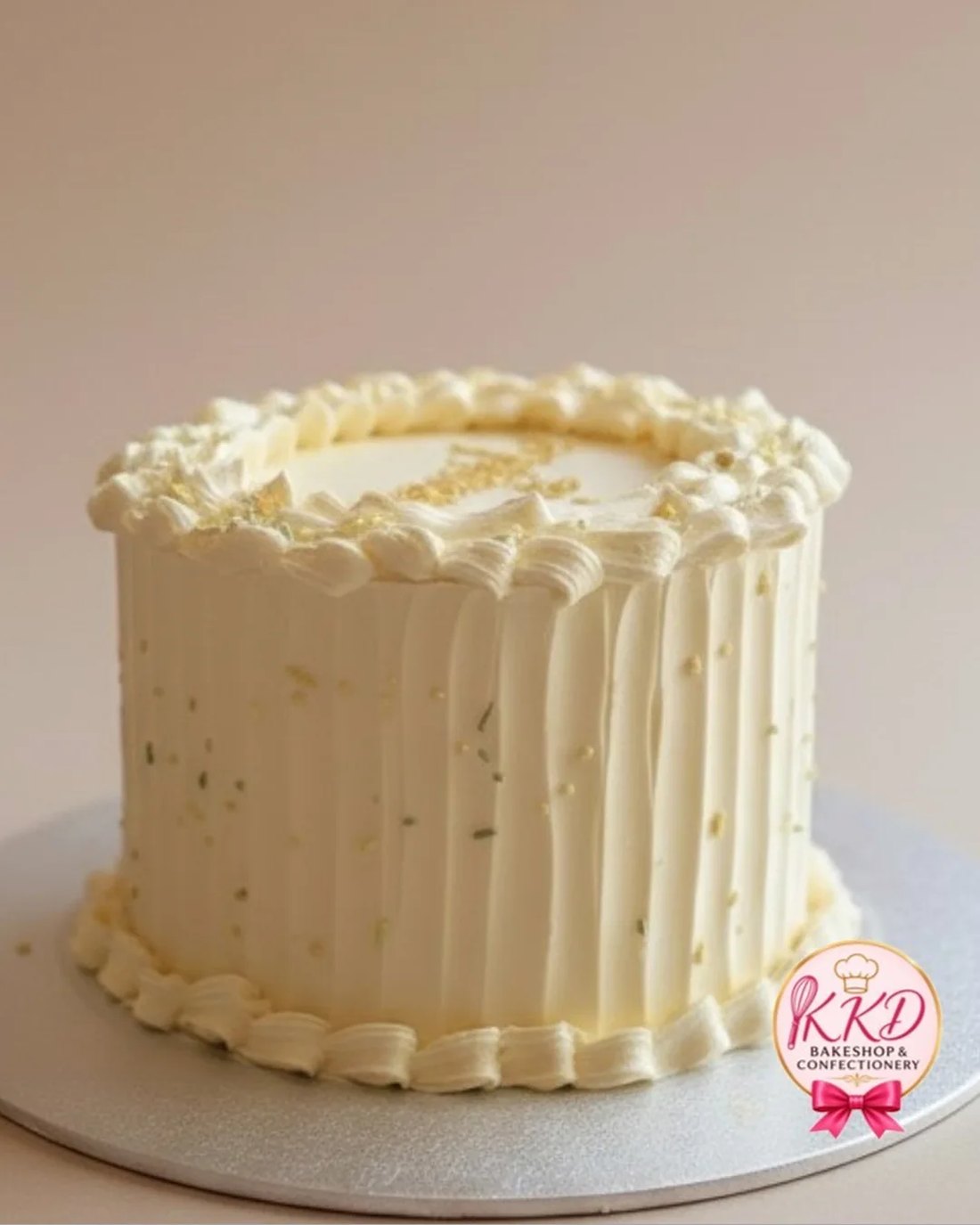 An ivory cake finished in vertical piped pleats with a piped shell border top and bottom and flecks of gold leaf