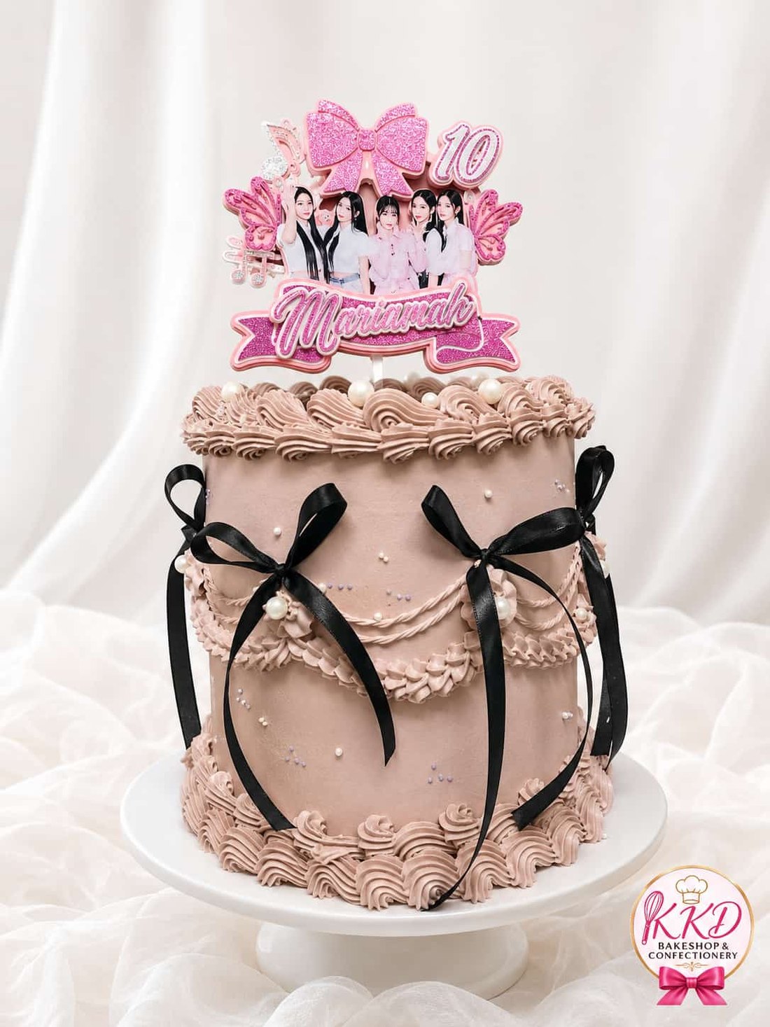 A tall mocha buttercream cake with vintage piping, sugar pearls, black satin bows and a personalised photo topper