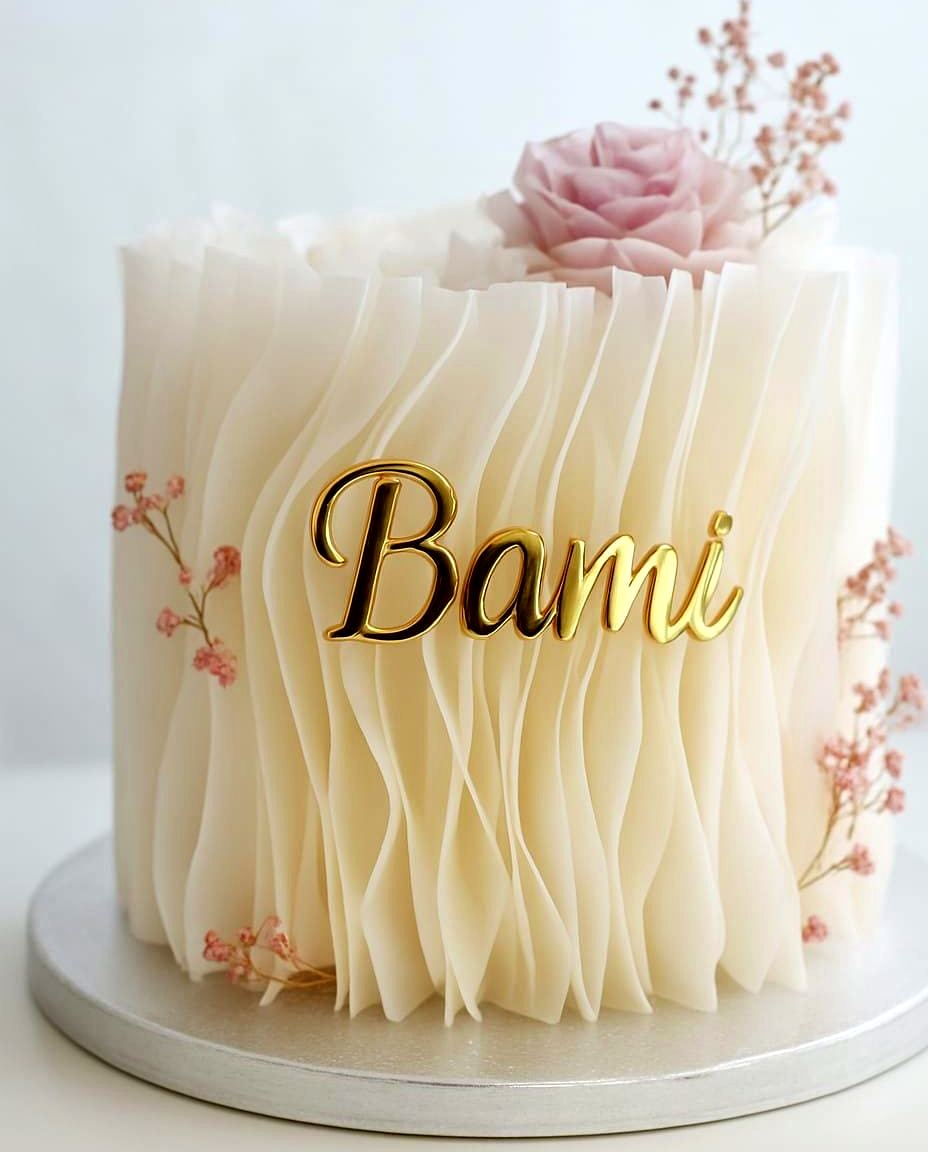 An ivory ruffle cake with a gold personalised name and sugar florals